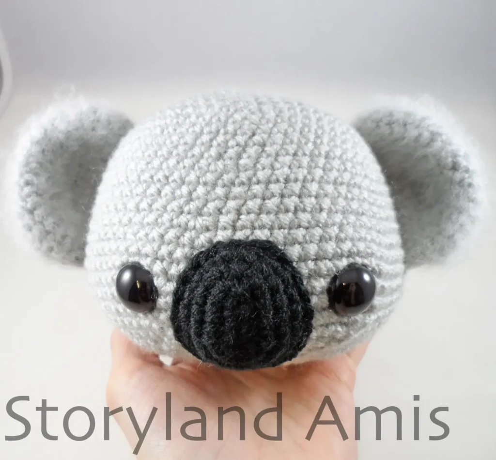 A hand holds up a crocheted koala head.