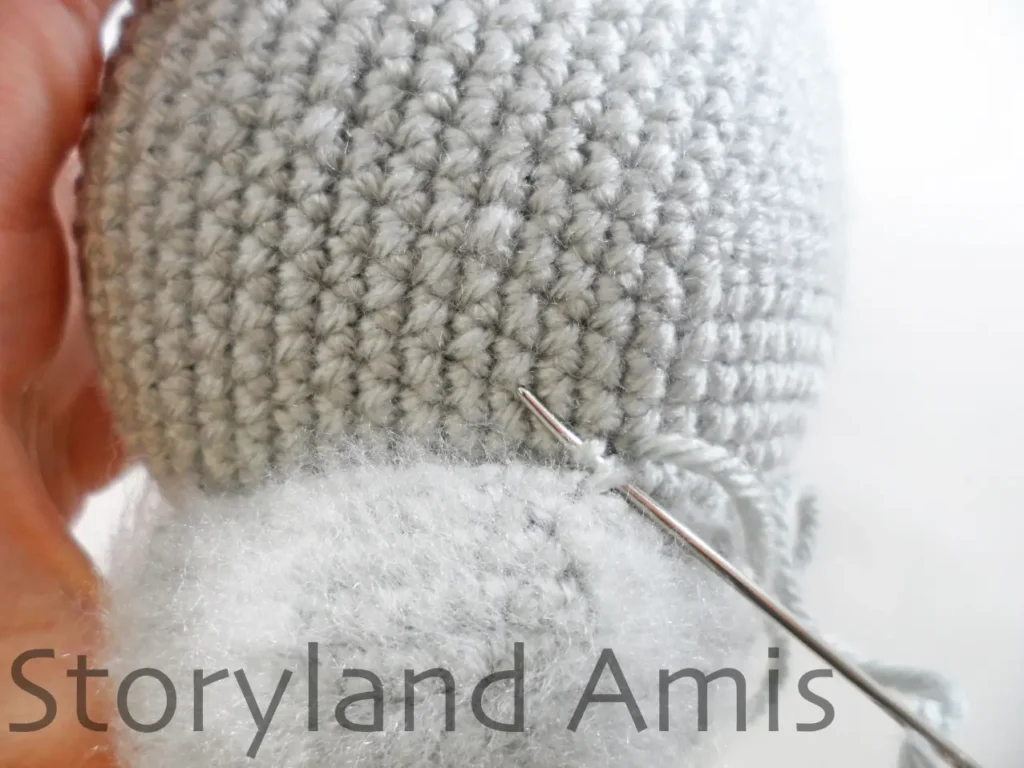 A close-up shows a crocheted ear being sewn to the head of an amigurumi koala using a tapestry needle and yarn tail.