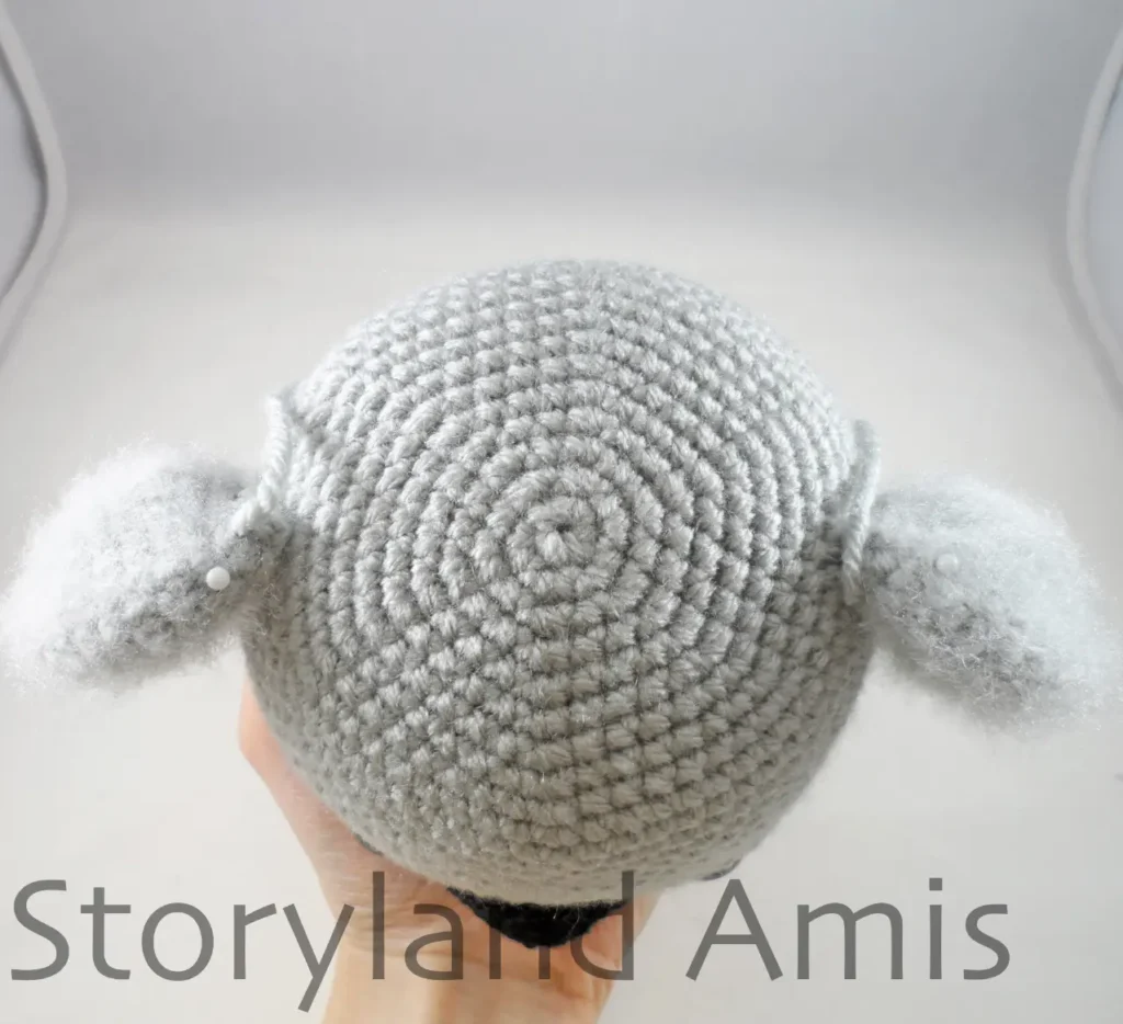 A hand holds a crocheted koala head, showing the top of the head.