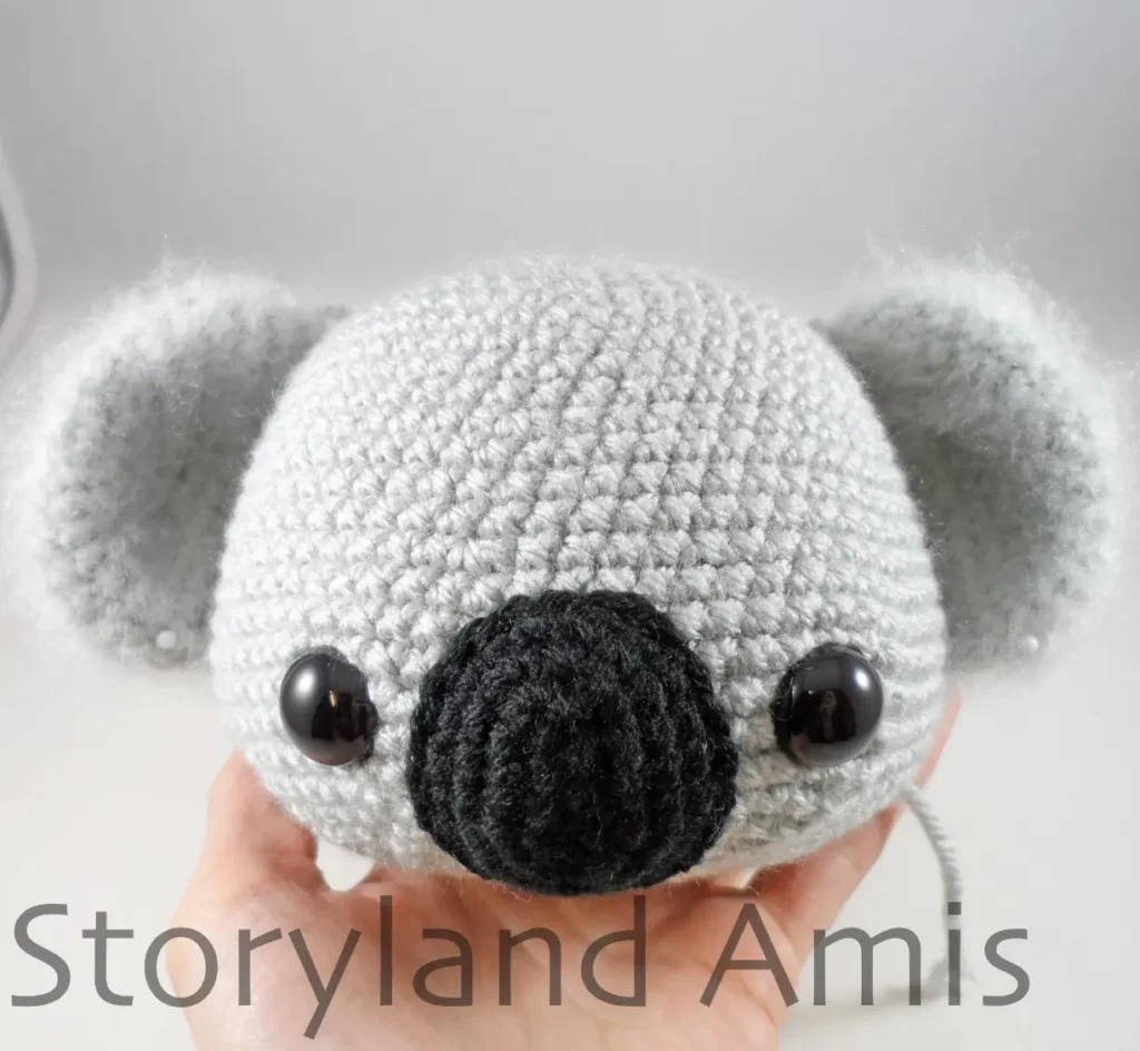 A hand holds up a crocheted koala head.