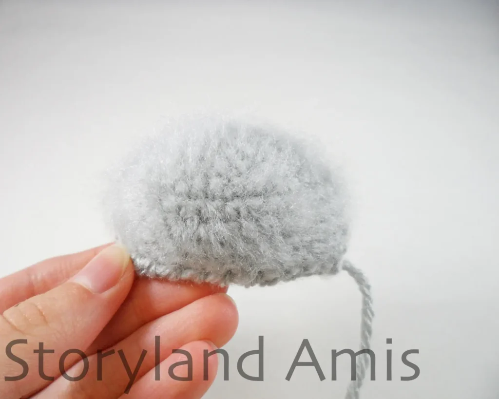 A hand holds up a fuzzy gray crocheted koala ear.