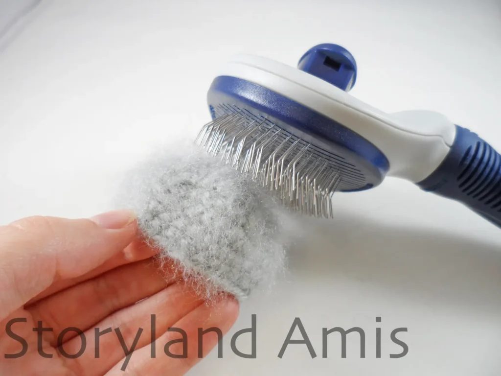 A close-up of a pet brush being used to brush a crocheted koala ear to make it fuzzy.