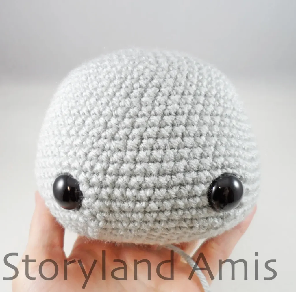 A hand holds a gray, partially finished amigurumi koala head.