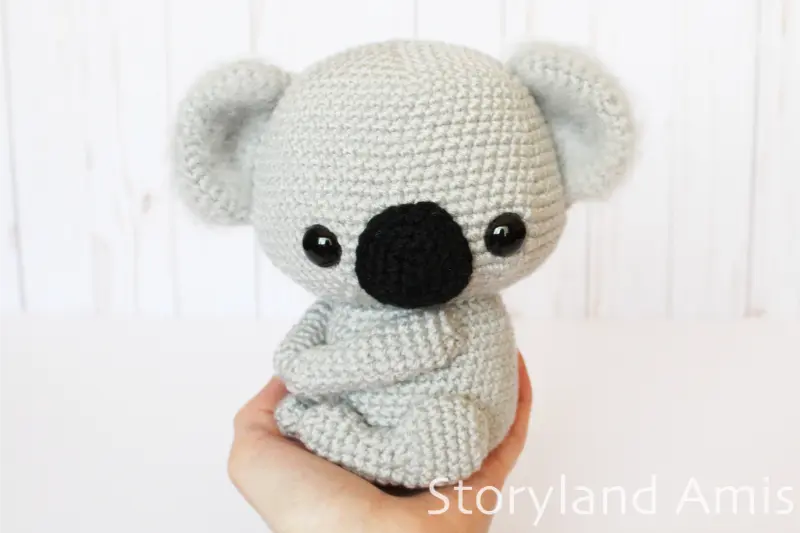 A hand holds a crocheted amigurumi koala against a white background.