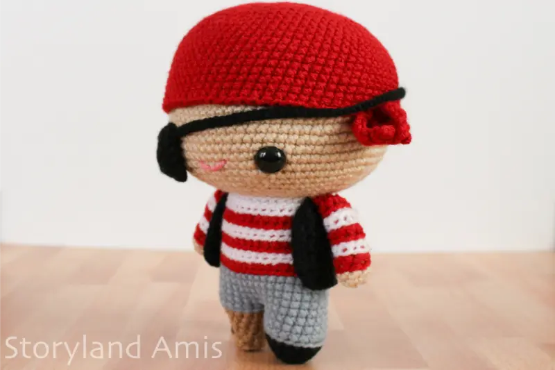 An amigurumi pirate doll stands on a wooden table.