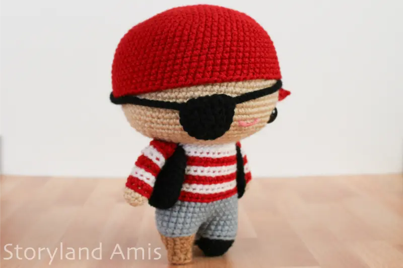 An amigurumi pirate doll stands on a wooden table.