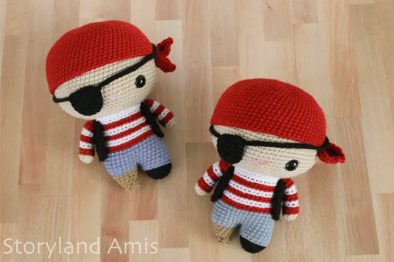 Two amigurumi pirate dolls lay on a wooden table.