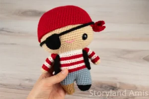 A hand holds an amigurumi pirate doll.