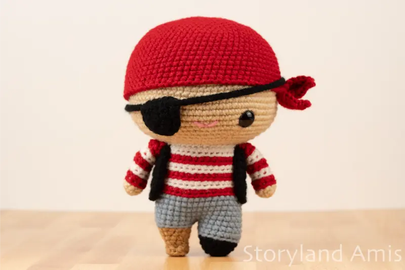 An amigurumi pirate doll stands on a wooden table.
