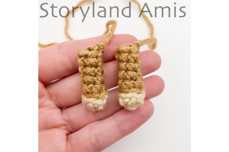 A hand holds two crocheted doll arms.