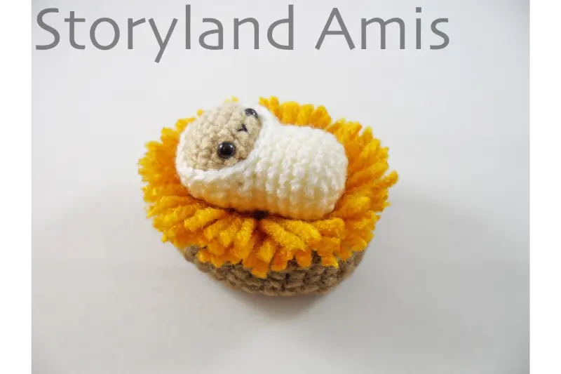 An amigurumi baby Jesus doll lies in a crocheted manger.