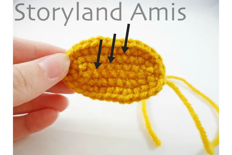 A hand holds a small yellow crocheted oval.
