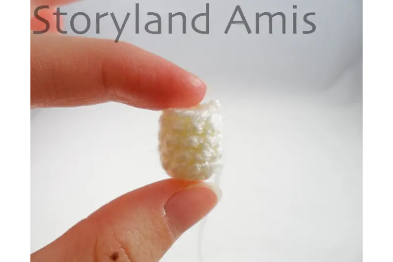 A hand holds up a tiny crocheted body for an amigurumi Baby Jesus doll.