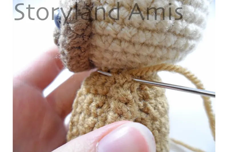 A close-up of an arm being sewn to the body of an amigurumi doll using a tapestry needle.