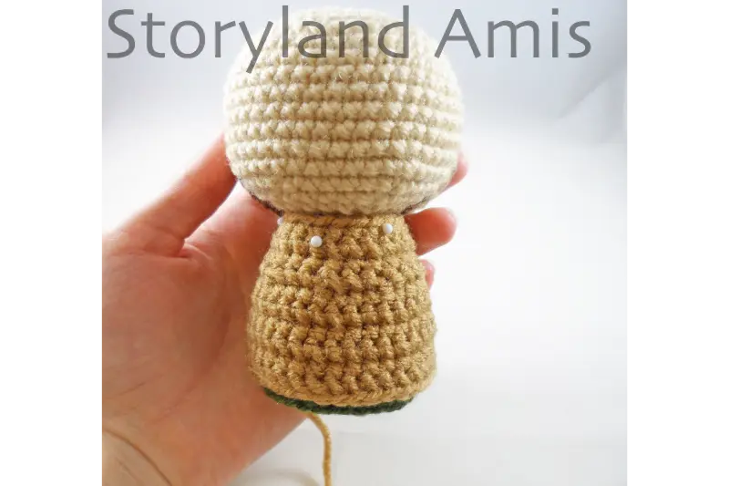 The backside of a partially finished amigurumi Joseph doll for a crocheted Nativity set is shown being held by a hand.