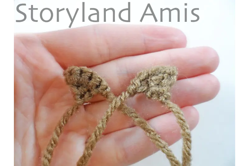 A hand holds two small brown, triangular crocheted pieces.
