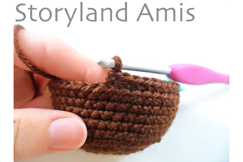 A hand demonstrates how to crochet into the back loops only using a pink crochet hook.