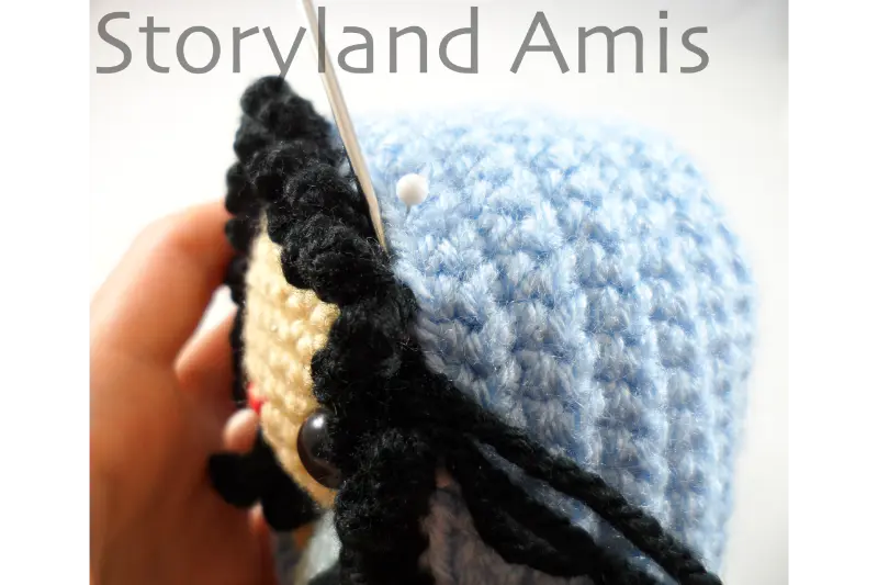 A close-up of a headdress being sewn to the head of an amigurumi doll using a tapestry needle.