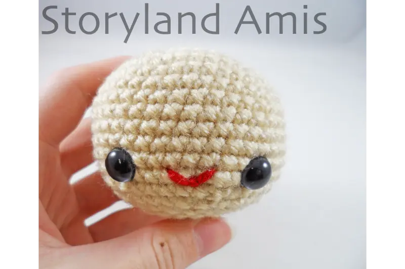 A hand holds up a crocheted doll head.