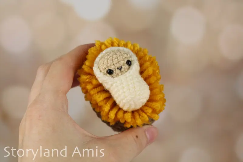 A hand holds an amigurumi baby Jesus in a crocheted manger.