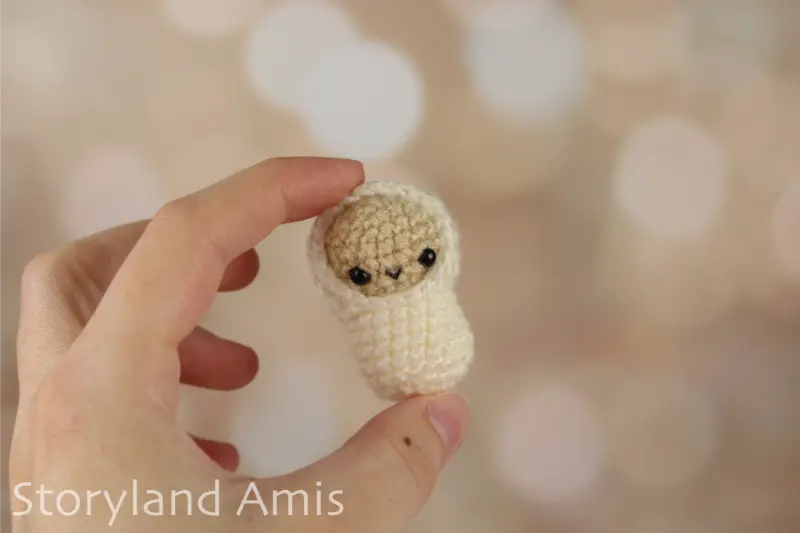 A hand holds up a tiny Baby Jesus amigurumi doll.