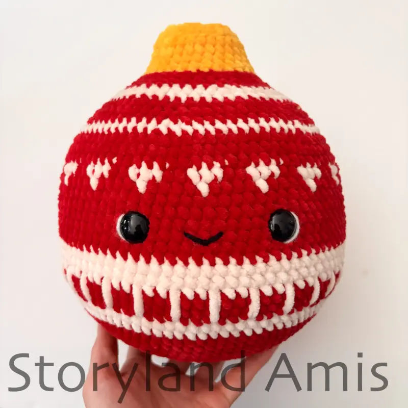 A hand holds up a large, round crocheted red Christmas ornament with a white design.