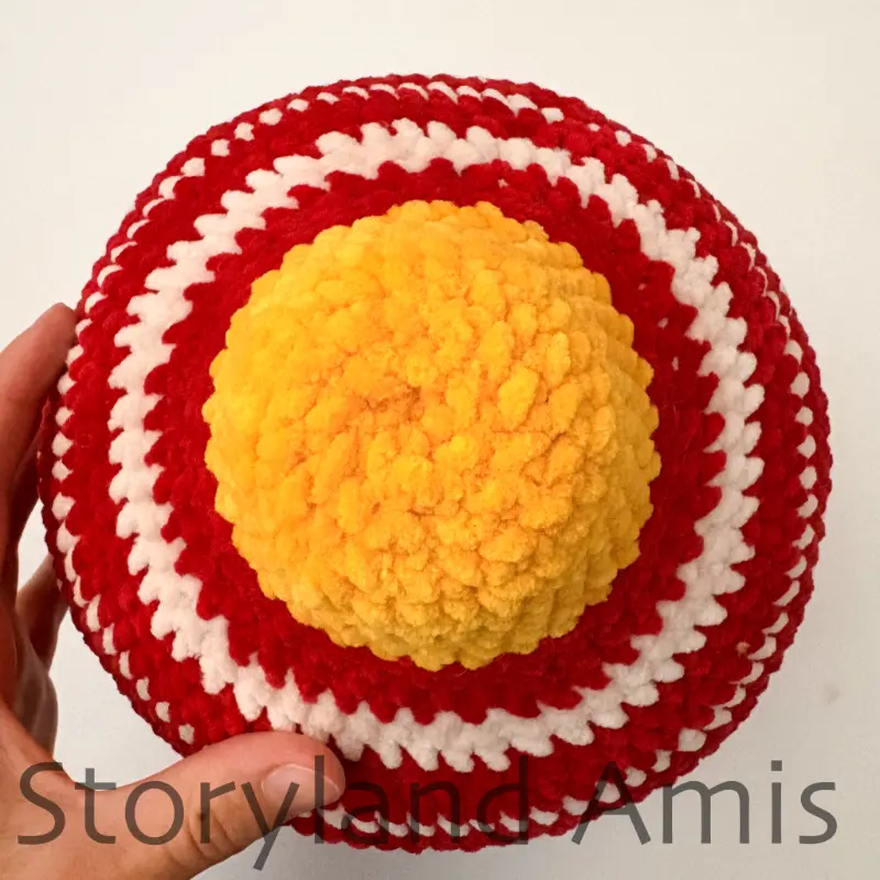 A close-up of the top of a crocheted amigurumi Christmas ornament is shown from the top.