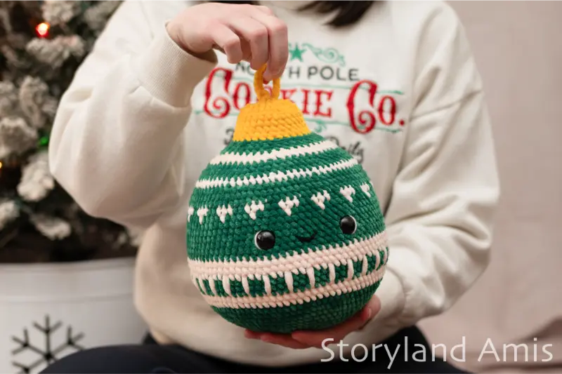A girl holds a green crocheted Christmas ornament with a white design.