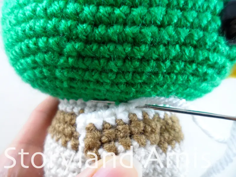 A close-up showing a hand sewing a crocheted wing to the body of an amigurumi duck using a tapestry needle.