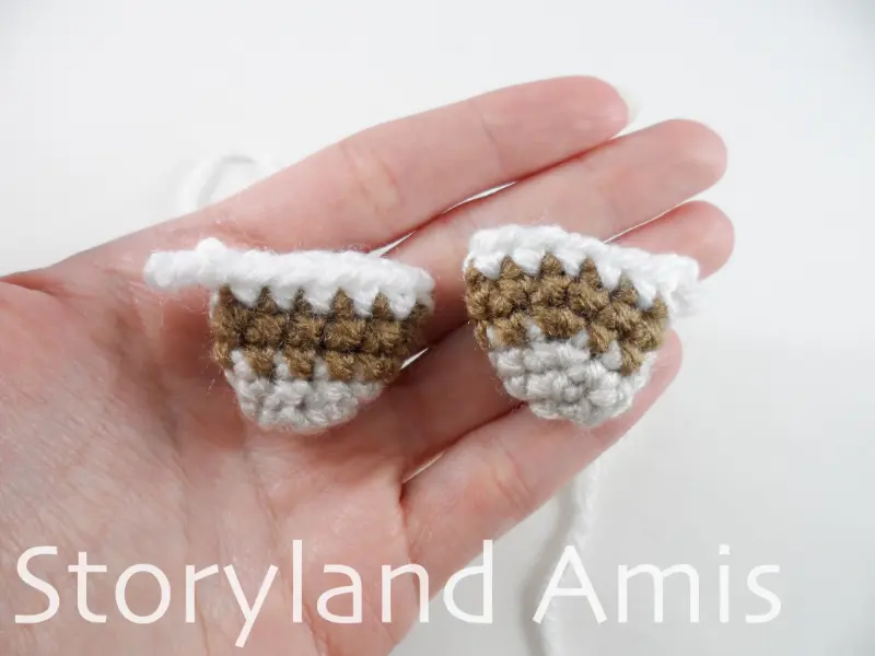 A hand holds two small, crocheted wings for an amigurumi mallard duck.