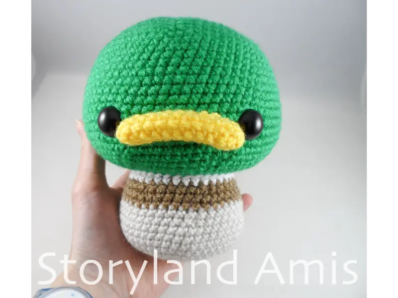 A hand holds a partially completed amigurumi mallard duck.