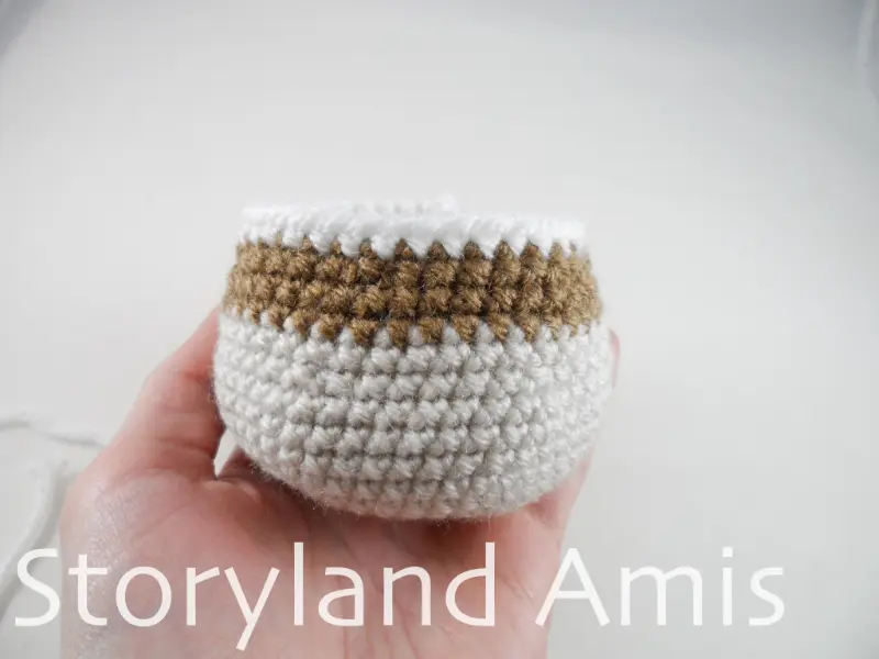 A hand holds up a crocheted body for an amigurumi mallard duck.
