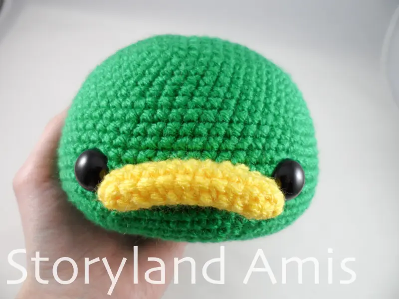 A hand holds an amigurumi duck head.