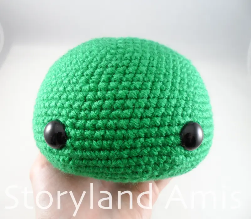 A hand holds a partially completed crocheted green duck head.