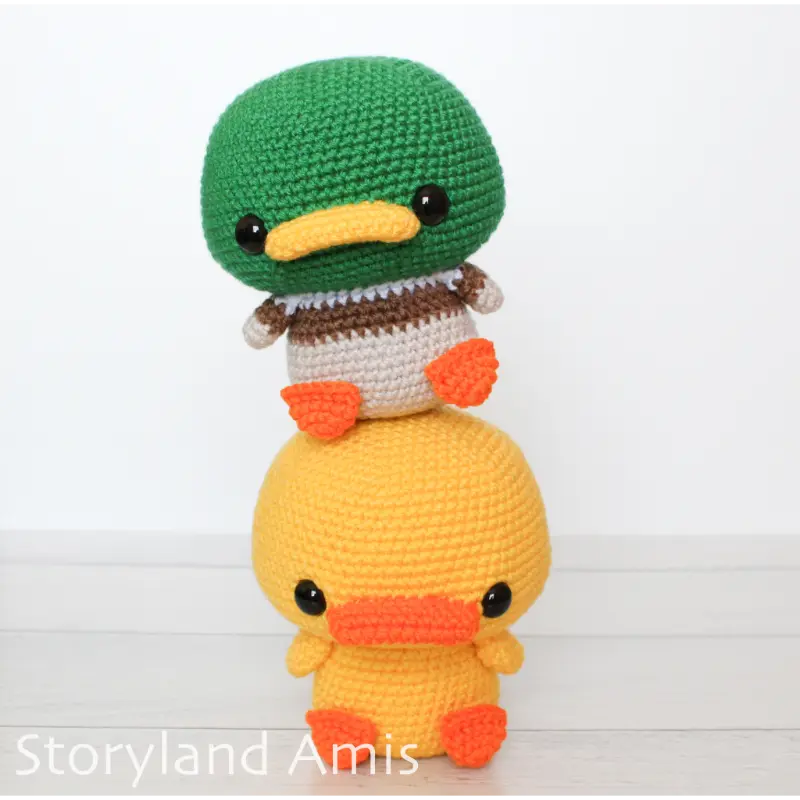 Two amigurumi ducks, one on top of the other, sit on a wooden table.