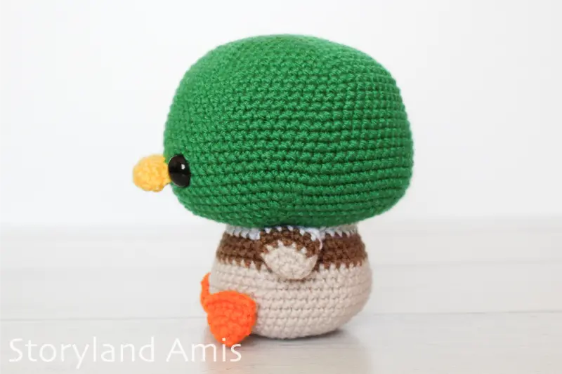 An amigurumi mallard duck sits on a wood table.