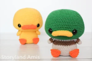 Two crocheted amigurumi ducks sit on a wooden table.