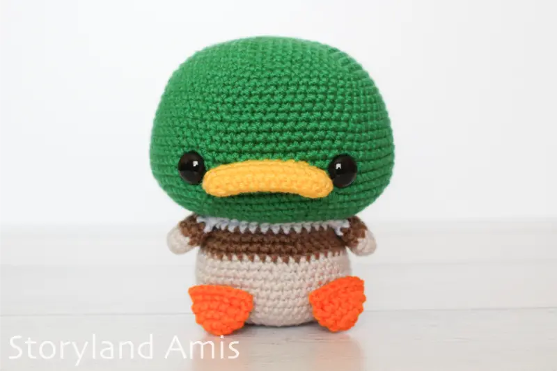 An amigurumi mallard duck sits on a wooden table.