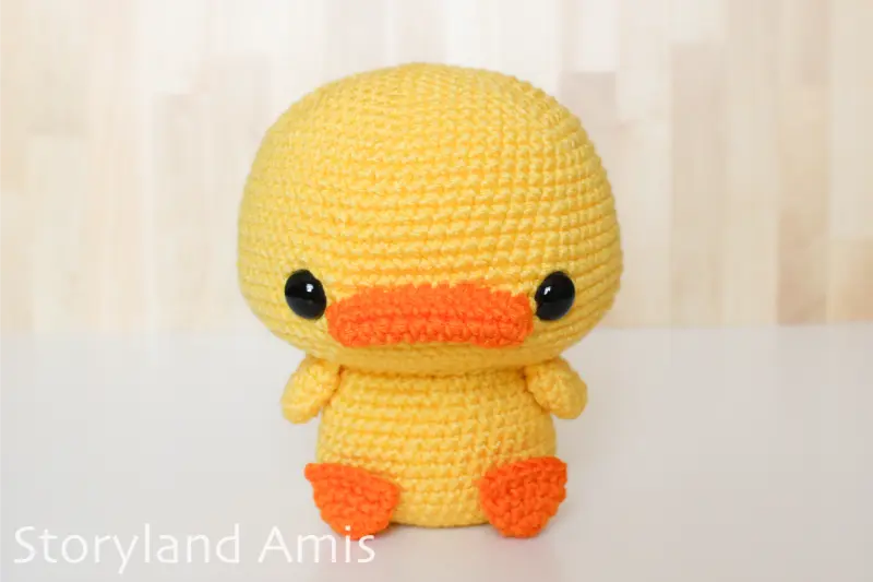 A yellow amigurumi duck sits on a white table.