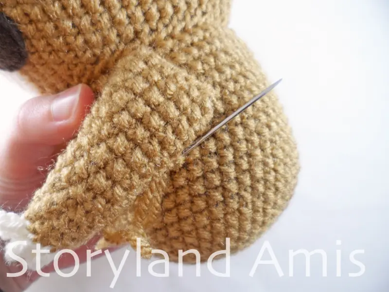 A close-up of a tapestry needle being used to to sew a crocheted arm to an amigurumi sloth body.