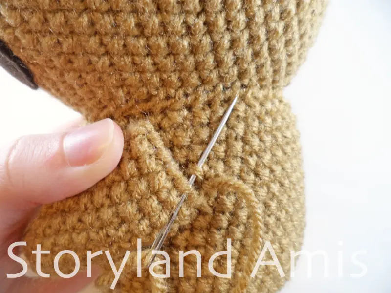 A close-up of a tapestry needle being used to sew a crocheted arm to an amigurumi sloth body.