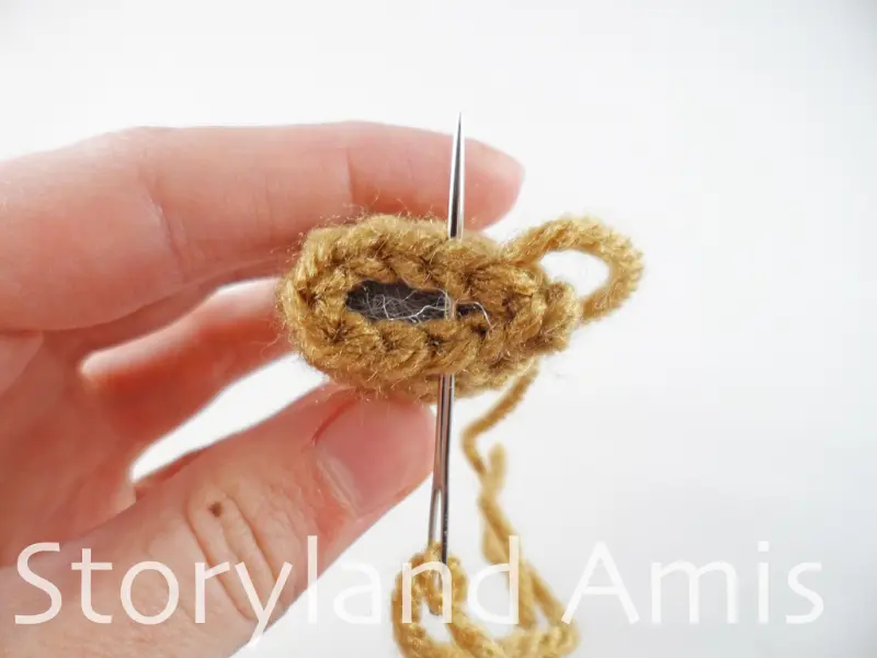 A close-up of a tapestry needle being used to sew the opening closed on a brown crocheted sloth arm.