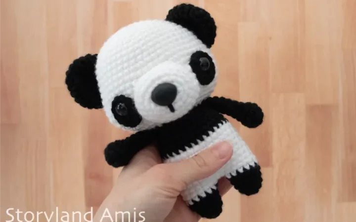 A hand holds a crocheted black and white panda amigurumi toy against a wooden background.
