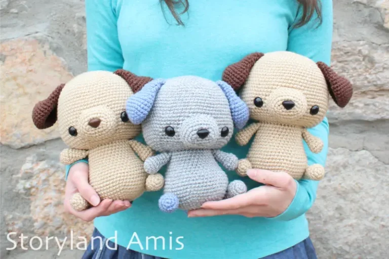 A girl wearing a blue turquoise shirt holds three crocheted amigurumi puppy dogs in her arms. Two of the dogs are tan with dark brown ears and one is gray with blue ears.