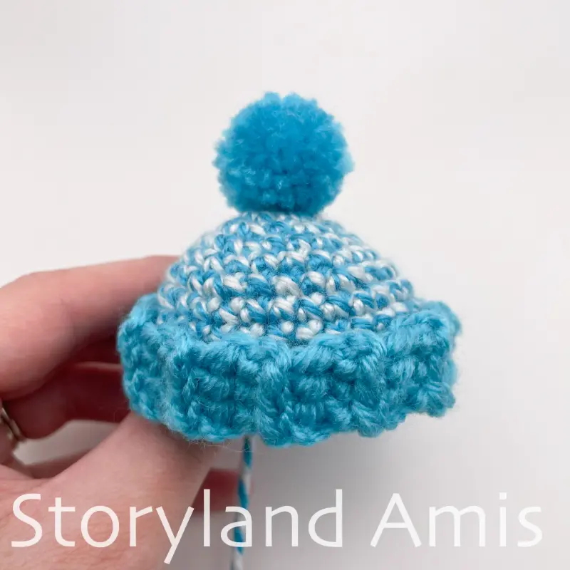 A hand holds a small blue crocheted stocking cap.