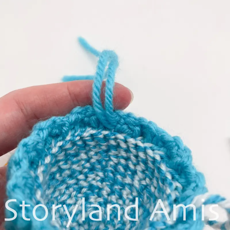 A close-up of two yarn tails coming out of the edge of a small blue crocheted stocking cap.