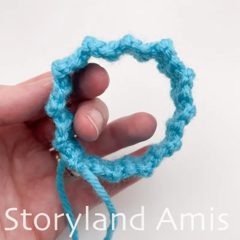 A hand holds a blue crocheted circular band.