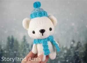 A hand holds an amigurumi polar bear wearing a blue crocheted hat and scarf.