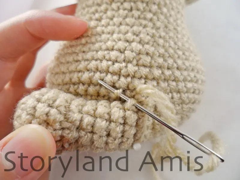 A close-up of a silver tapestry needle being used to sew a crocheted leg to the body of an amigurumi puppy dog.