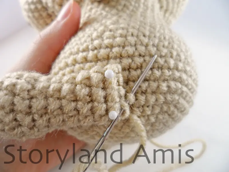 A close-up of a silver tapestry needle being used to sew a crocheted leg to the body of an amigurumi puppy dog.